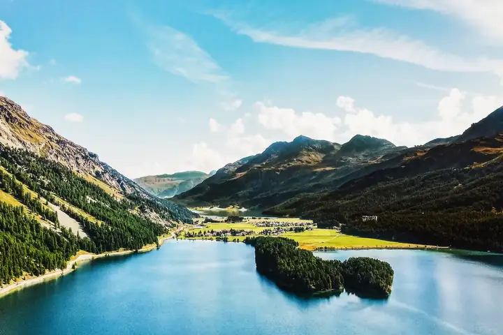 An alpine lake with a wooded peninsula and mountains — Bright Slide 50